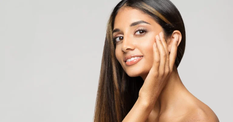 A young woman with glowing skin and long dark hair gently touches her face, smiling softly against a light gray background in Yuma, AZ, after EuroThread treatment.